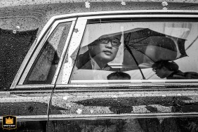 In Hangzhou, China, a groom patiently waits inside a car in the rain, with raindrops creating a serene ambiance on the car window.